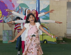Girls with outstretched arms dance on a green floor in front of a colourful wall in the Bekaa Valley, Lebanon.