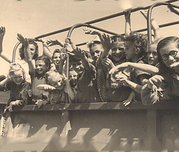 A group of cheerful children wave from a Caritas truck at the Auhof summer camp in 1946