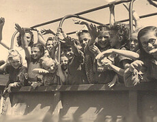 A group of cheerful children wave from a Caritas truck at the Auhof summer camp in 1946