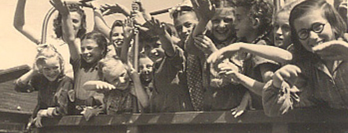 A group of cheerful children wave from a Caritas truck at the Auhof summer camp in 1946