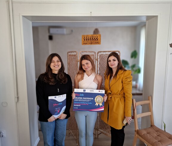 Three women stand side by side in a room, holding a certificate and a folder.