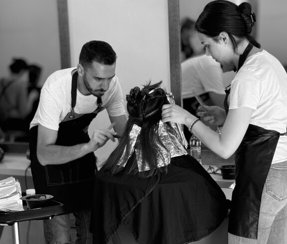 Two people are jointly carrying out a hairdressing treatment on a seated person.