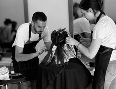 Two people are jointly carrying out a hairdressing treatment on a seated person.