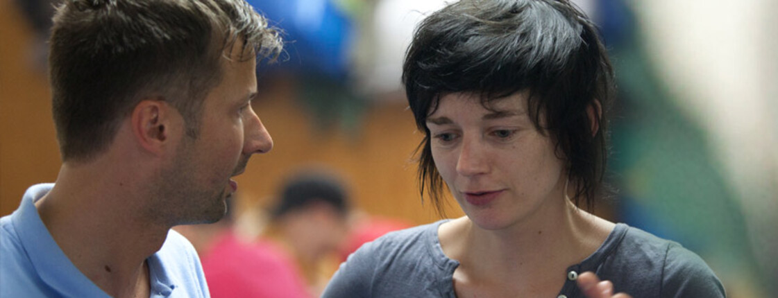A woman with short black hair and a man are talking. 