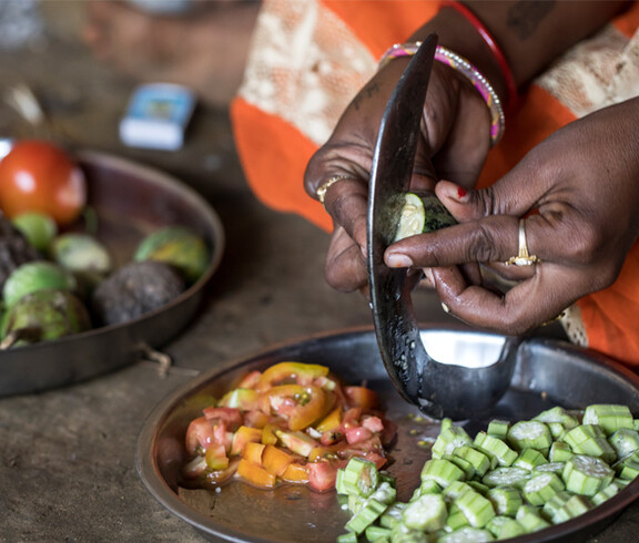 Close-up: A woman cuts a cucumber with a sickle, surrounded by further vegetables