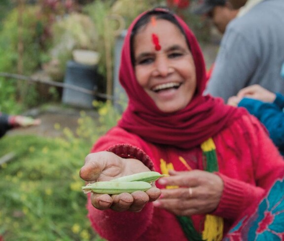 Laughing woman in red clothing holds fresh green legumes towards the camera