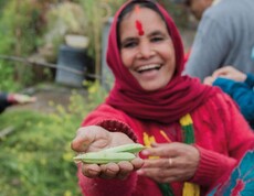 Laughing woman in red clothing holds fresh green legumes towards the camera