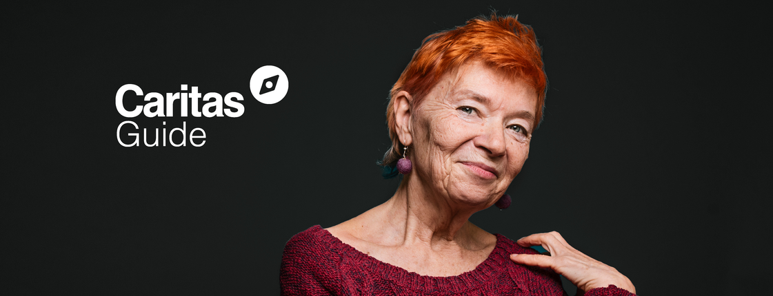 A portrait of a woman is shown against a black background. She is an older woman with a smile and short red hair. In the upper left corner is the Caritas Wegweiser logo.