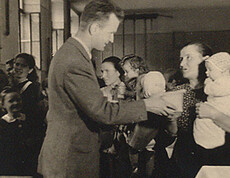 A man hands a package of sugar to a mother with a child—a scene from a Caritas food distribution in 1946