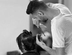 A person is cutting the hair of a seated individual with scissors.