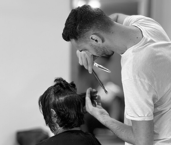 A person is cutting the hair of a seated individual with scissors.