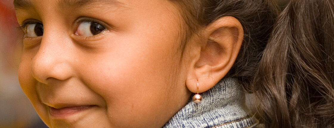 A girl wearing an earring smiles towards the camera from the side.